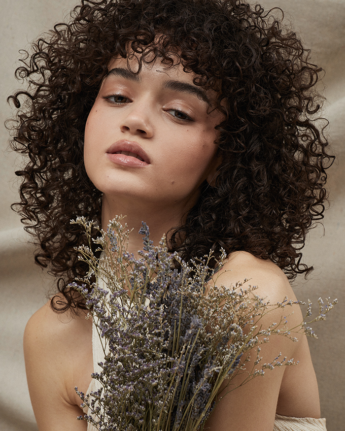 Dunkelhaarige Frau mit definierten Locken hält Trockenblumen in der Hand, natürliches Styling und gepflegte Locken im Fokus.