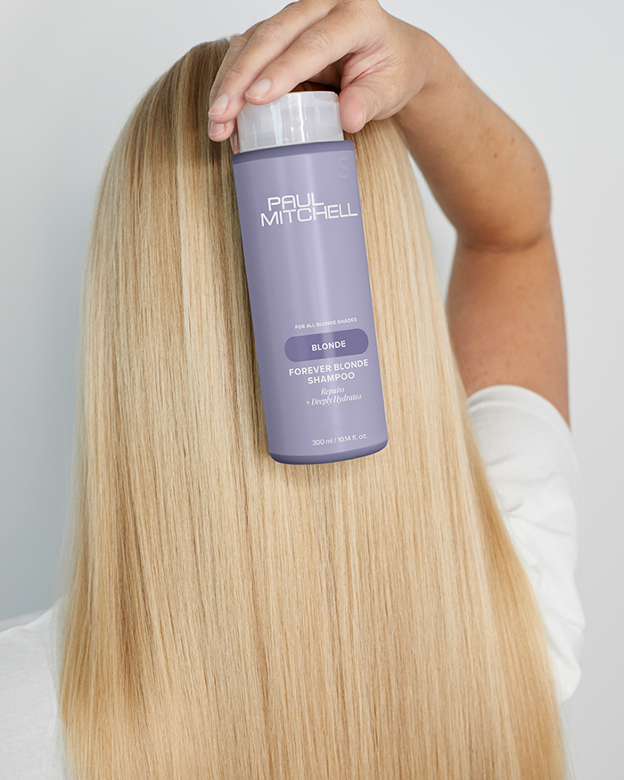 Foto blonder Haare von hinten mit einer Hand, welche das Shampoo der Paul Mitchell Blond Pflege – Für perfektes Blond hält