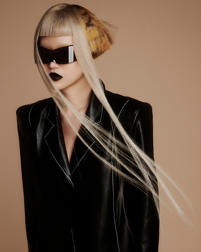 Foto der Avantgarde Kollektion "Luminary" von Bernadette Beswick. Weibliches Model mit schwarzem Lederblazer & Sonnenbrille und einem futuristischen blonden Kurzhaarschnitt